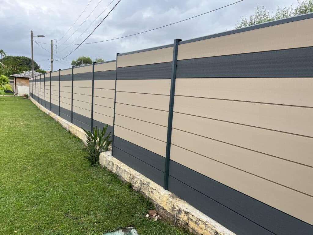 Longue clôture composite bicolore beige et gris anthracite, délimitant un jardin verdoyant avec pelouse et bordure en béton.